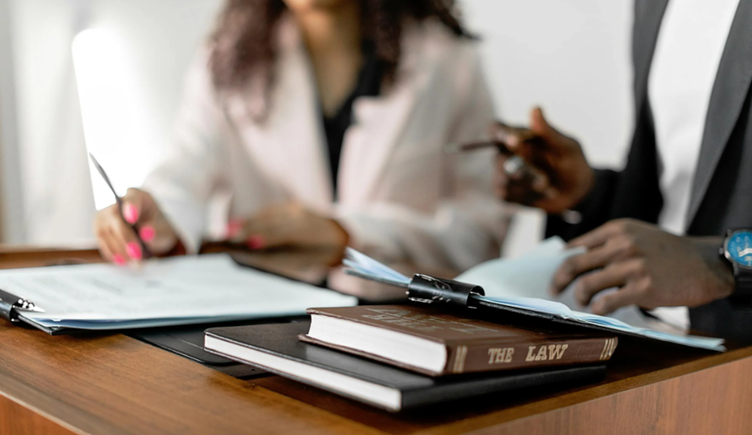 Two people reviewing legal documents at a desk with law books