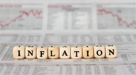 The word “Inflation” is written in wood letters shaped in dice on a background of papers that show statistics and graphs